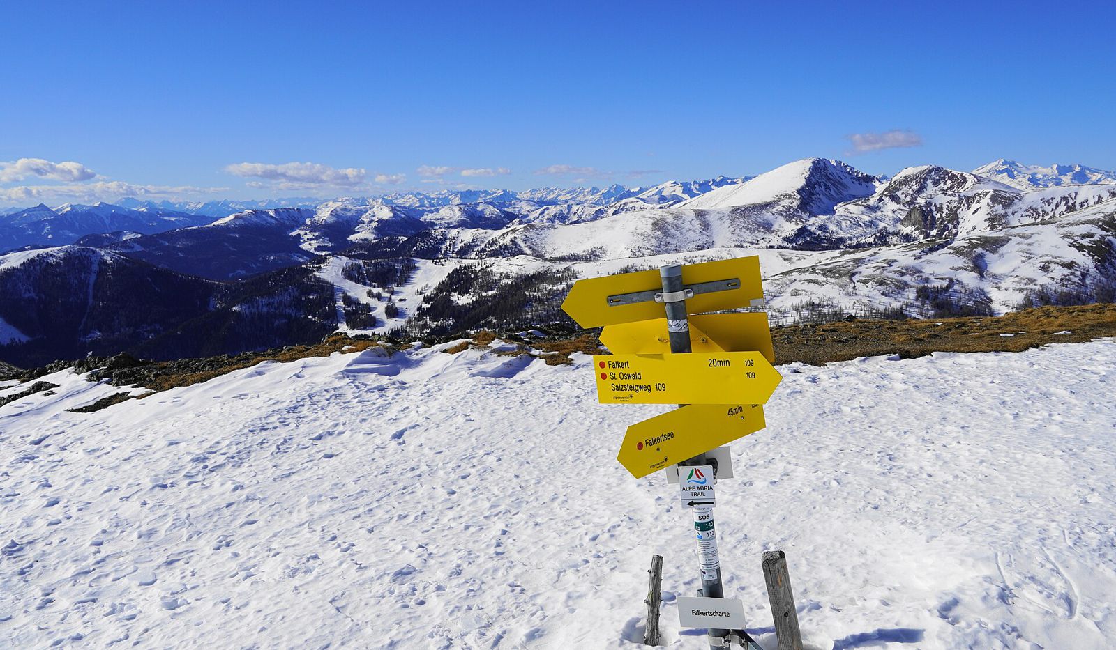 Hiking signs at the snowy Falkertscharte pass with a wide Nockberge panorama